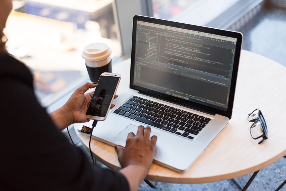 A person using a phone beside a laptop. Editorial stock photograph.